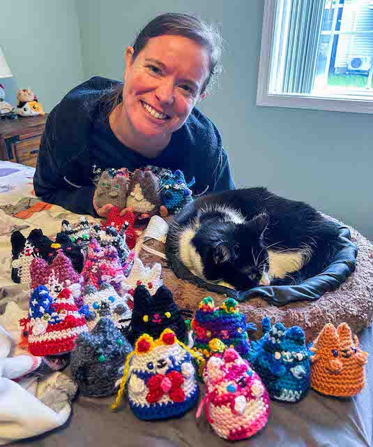 Brianna posing with a dozen kitty minis of various sorts, next to a real tuxedo cat curled in a cat bed | Kitten KaZoedle