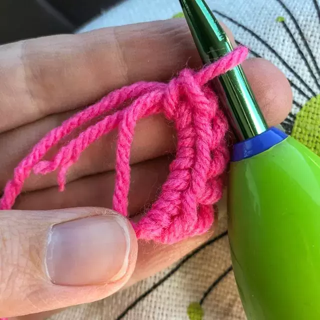 Close-up image of a crochet hook on a partially completed magic circle, with pink stitches held in-hand | Kitten KaZoedle